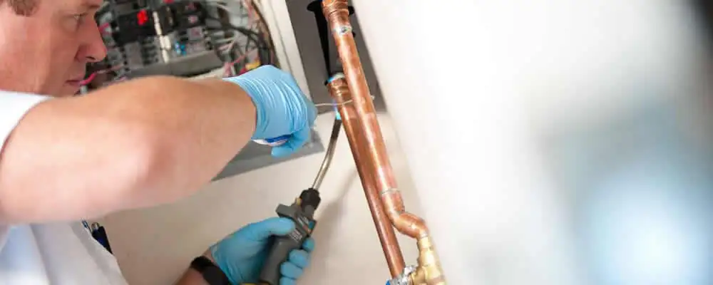 Water heater repair technician testing copper pipe connections and controls in Kissimmee, FL